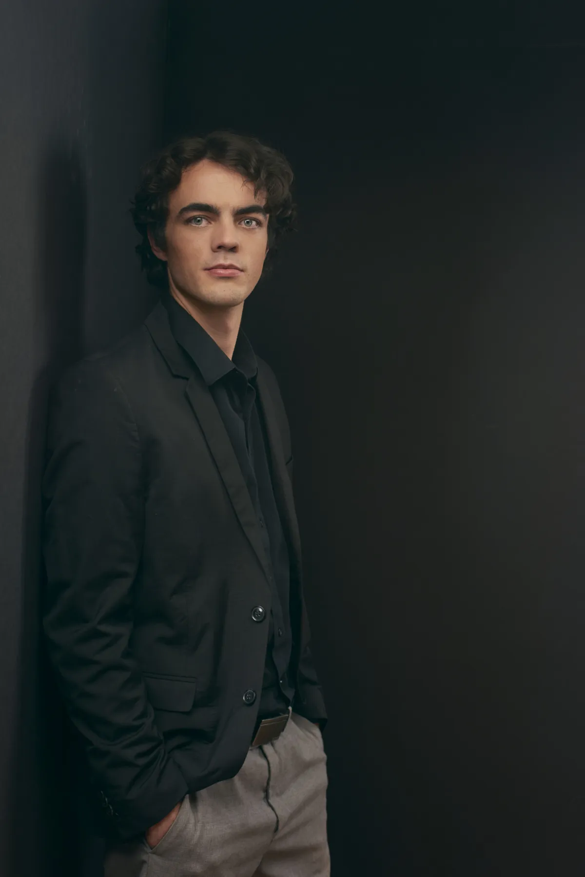 Professional man young man with dark hair wearing black shirt, seated against matching background